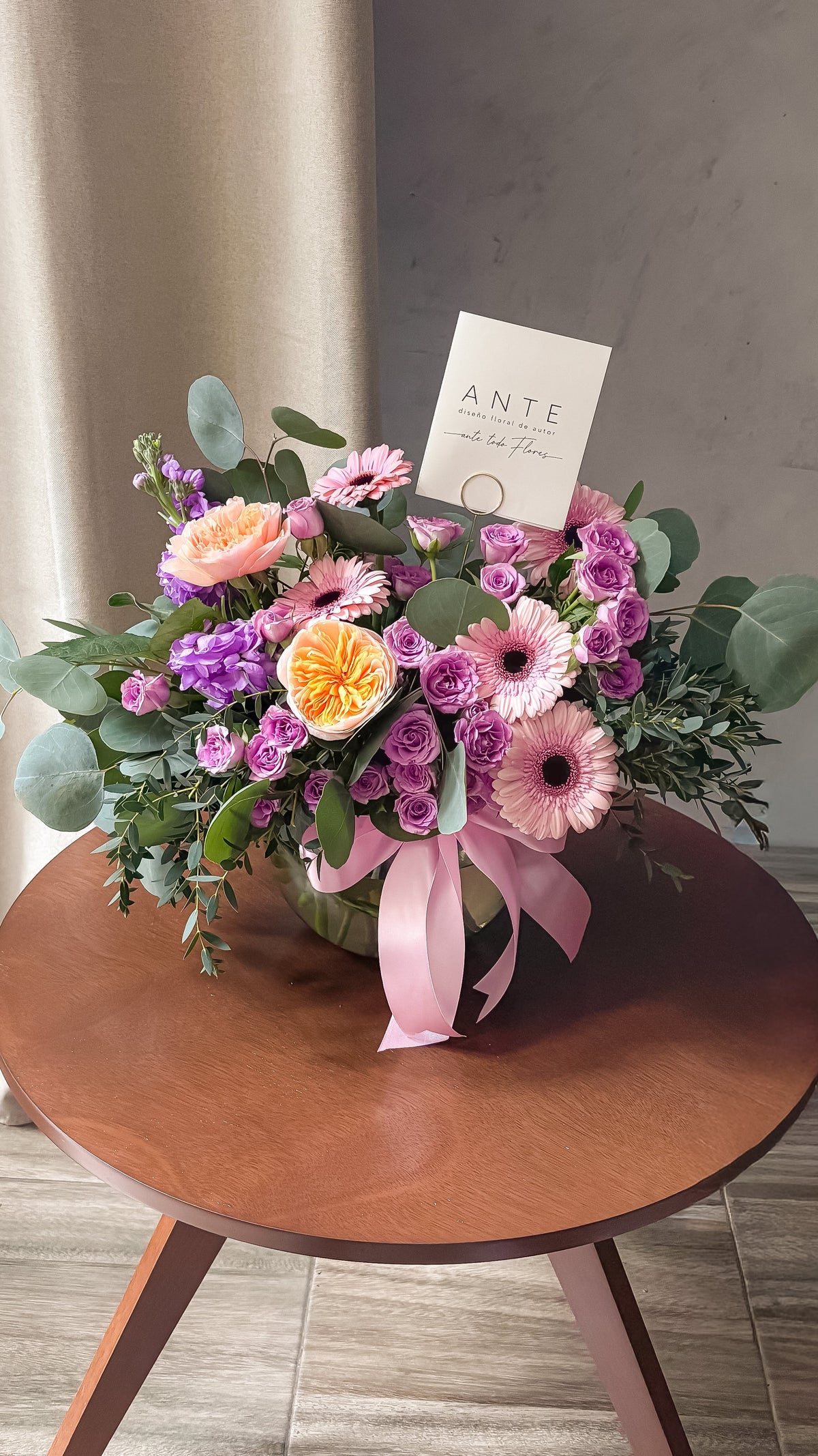 Arreglo floral con rosas inglesas juliet durazno, mini rosas lila, gerberas rosa y alhelí morado en florero de vidrio con moño rosa, entrega a domicilio CDMX