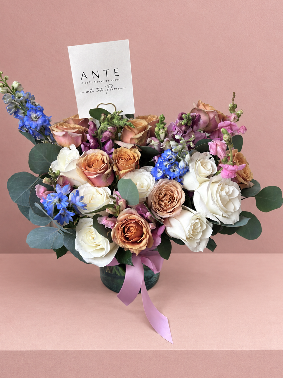 Arreglo floral con rosas terracota, rosas blancas, delphinium azul y alhelí lila en florero de vidrio con moño lila, entrega a domicilio CDMX