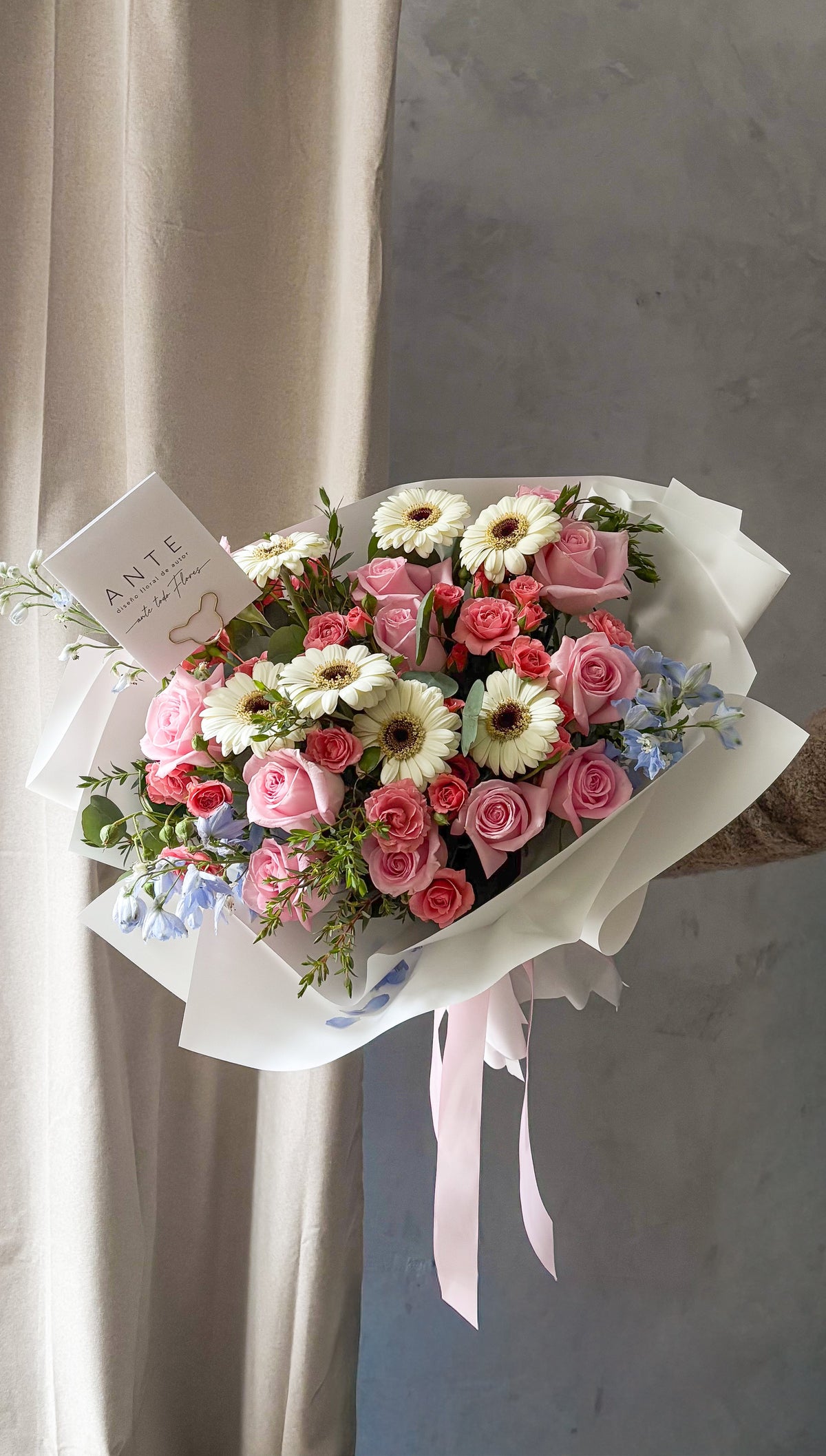 Ramo de rosas rosadas, mini rosas coral, gerberas blancas y delphinium azul claro con eucalipto en envoltura blanca con listón rosa, entrega a domicilio CDMX
