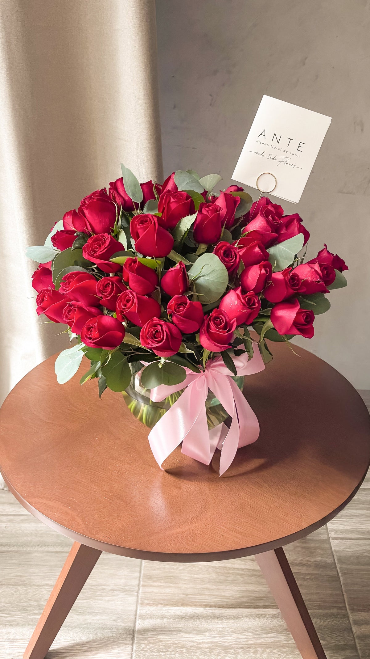 Arreglo de 50 rosas rojas con eucalipto en florero de vidrio redondo con moño rosa, entrega a domicilio CDMX