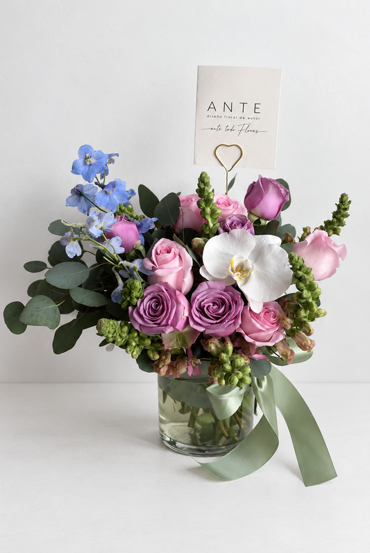 Arreglo floral con delphinium azul, rosas rosas y moradas, y orquídea blanca en florero de vidrio, entrega a domicilio CDMX