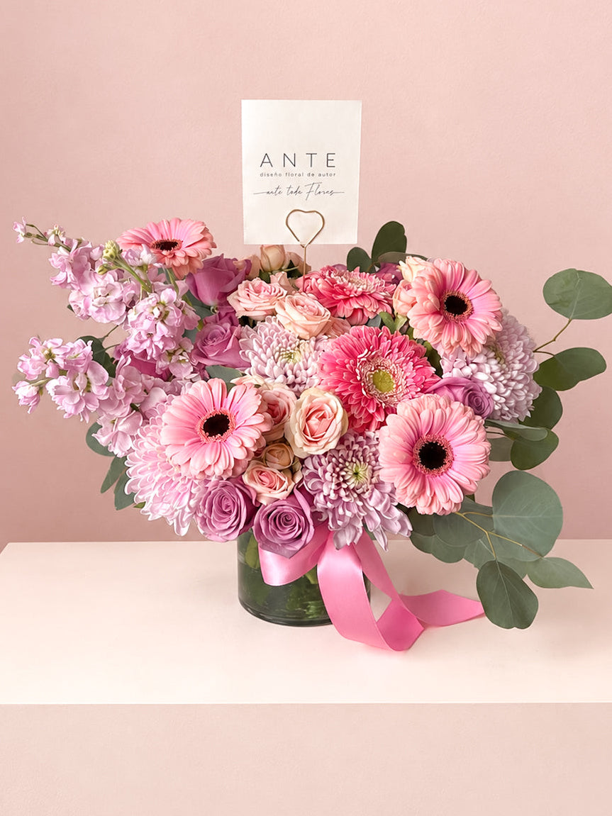 Arreglo floral con gerberas rosas, crisantemo lila, alhelí y rosas en florero de vidrio con moño rosa, entrega a domicilio CDMX