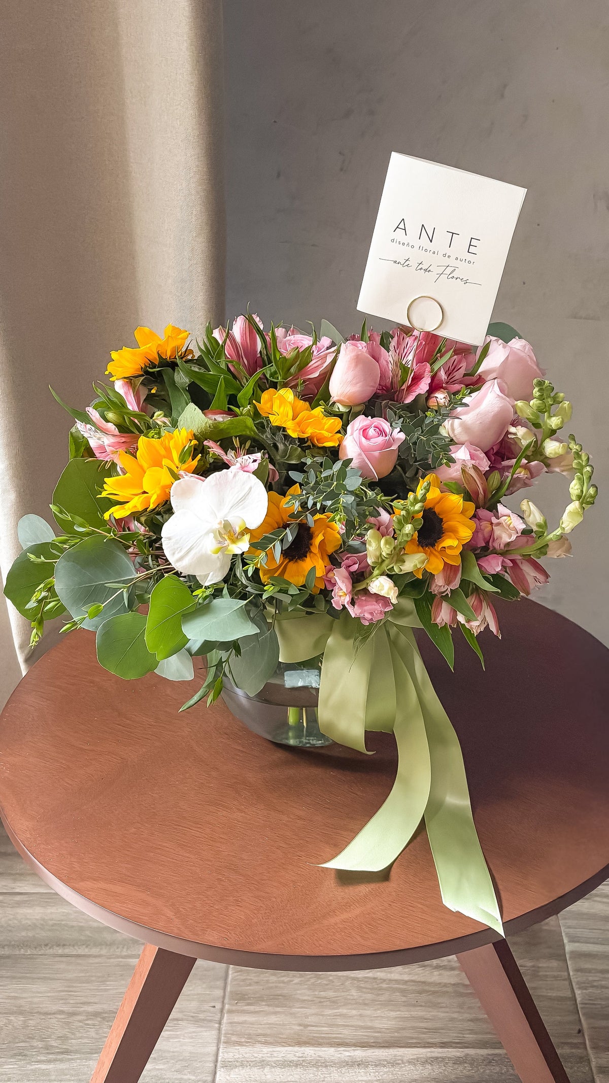 Arreglo floral con girasoles, rosas rosas, alstroemerias, perritos y orquídea blanca en florero de vidrio con moño verde salvia, entrega a domicilio CDMX