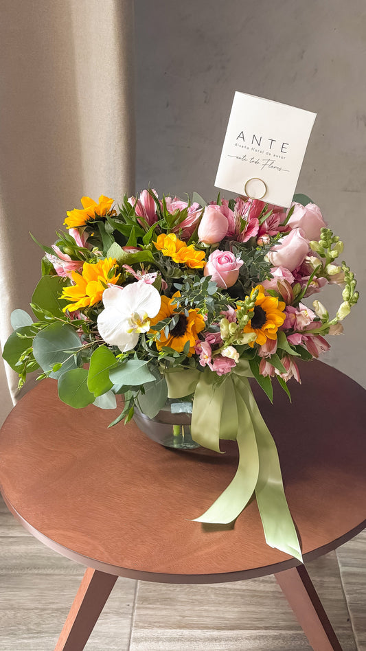 Arreglo floral con girasoles, rosas rosas, alstroemerias, perritos y orquídea blanca en florero de vidrio con moño verde salvia, entrega a domicilio CDMX