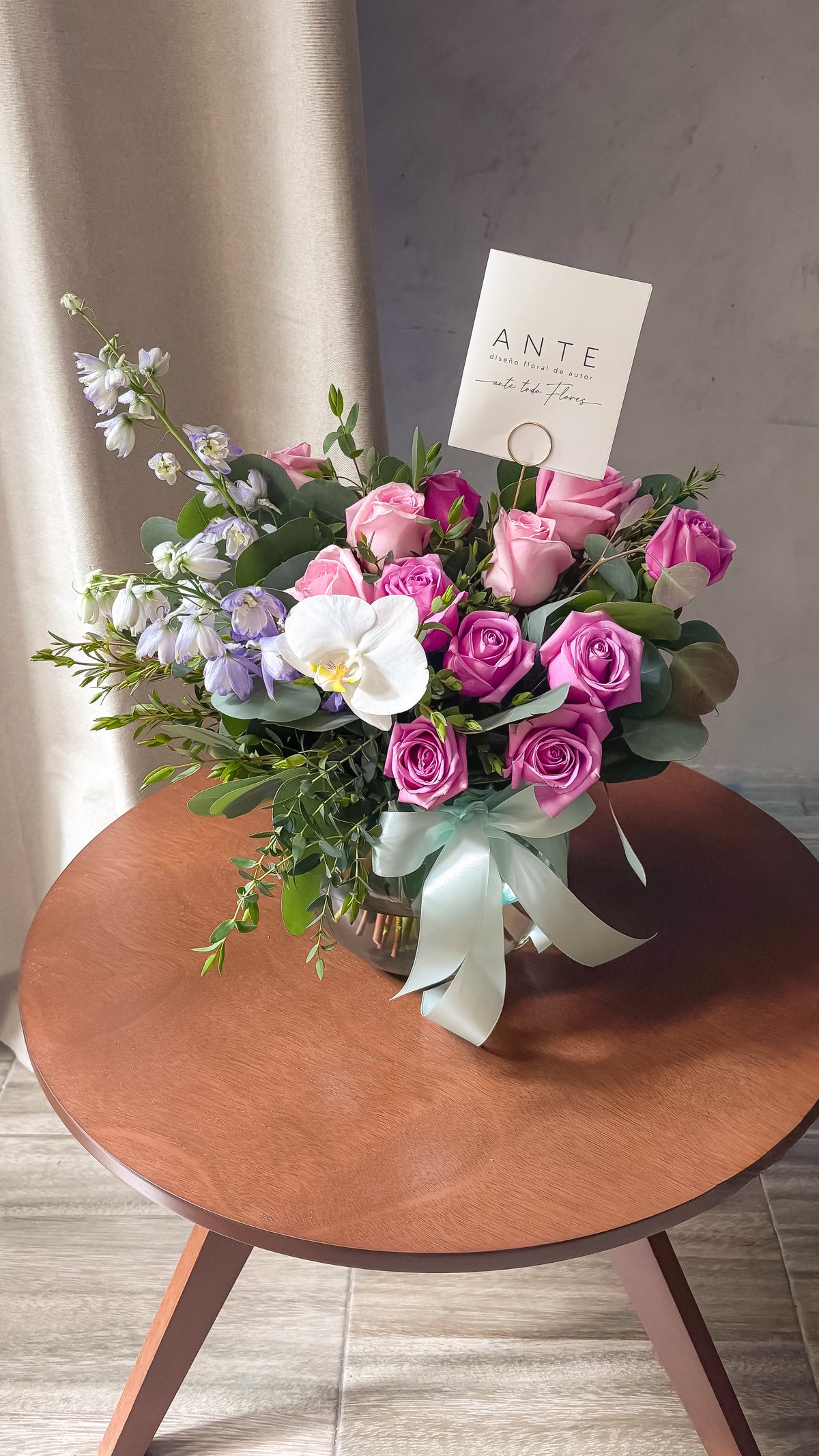 Arreglo floral con rosas moradas y rosas, delphinium lavanda y orquídea blanca en florero de vidrio con moño menta, entrega a domicilio CDMX