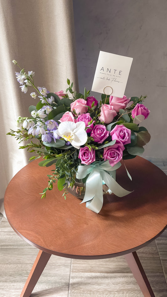 Arreglo floral con rosas moradas y rosas, delphinium lavanda y orquídea blanca en florero de vidrio con moño menta, entrega a domicilio CDMX