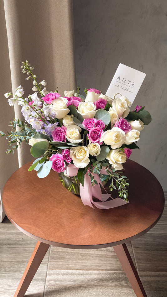 Arreglo de rosas blancas, mini rosas spray fucsia y delphinium lavanda con eucalipto en florero de vidrio redondo con moño rosa palo, entrega a domicilio CDMX