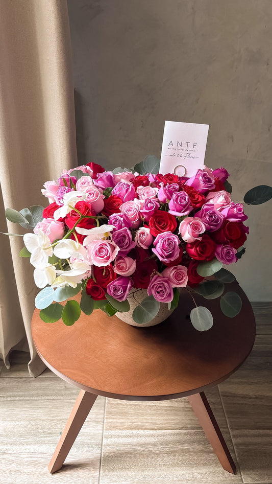 Arreglo de rosas rojas, rosas y moradas con orquídeas blancas en cascada en florero cerámico gris, entrega a domicilio CDMX
