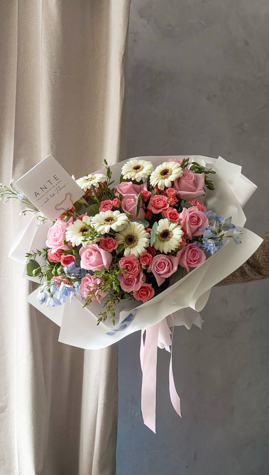Ramo de rosas rosadas, mini rosas coral, gerberas blancas y delphinium azul claro con eucalipto en envoltura blanca con listón rosa, entrega a domicilio CDMX